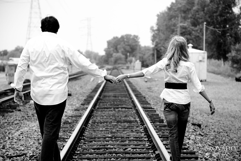 black and white photo of couple holding hands on traintracks