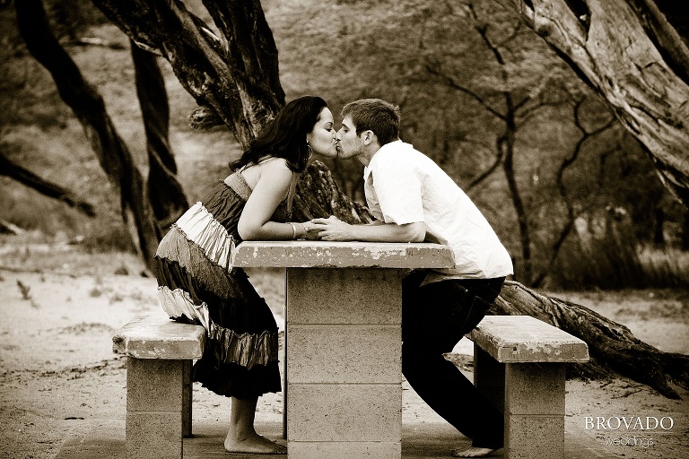 couple kiss from opposite sides of a picnic table in sepia tones